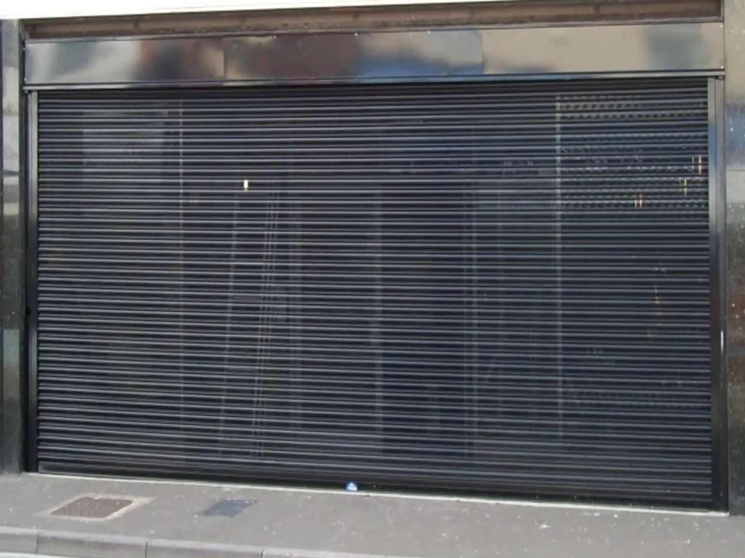 Ultradoor in black with perforated lath, fully enclosing a shopfrontwebp